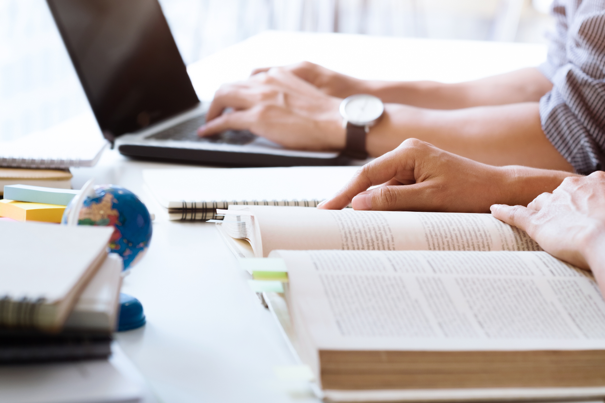 Two people studying. One on the laptop, the other in a book